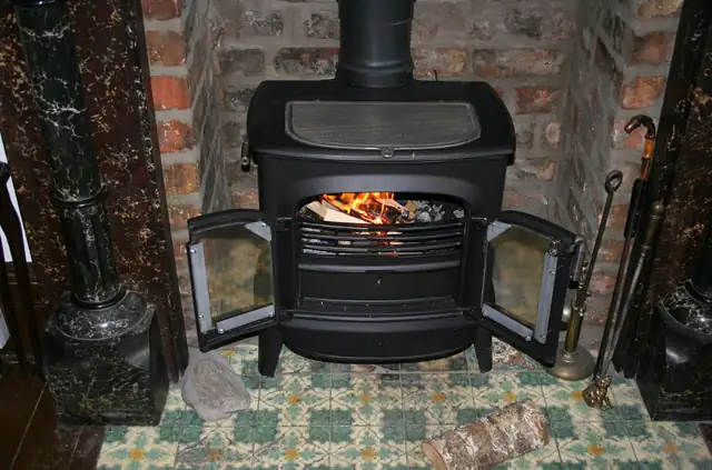 Cast iron wood burning stove, Newcastle Black cast iron wood burning stove with its doors open on a tiled hearth