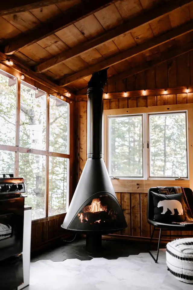 Black suspended fireplace in a wood-panelled living room with tall windows