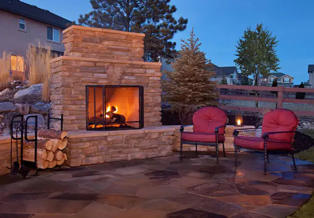 Stone outdoor fireplace on a garden patio with two red armchairs